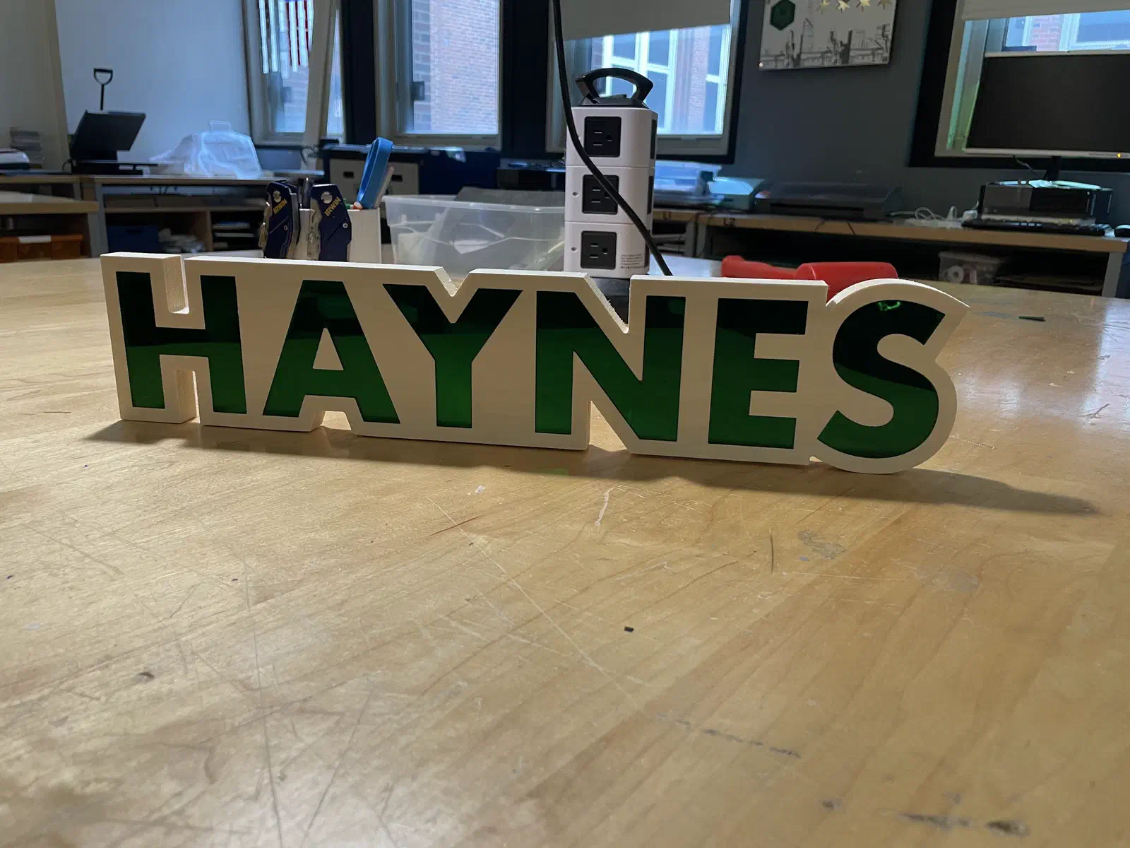 A freestanding name sign reading HAYNES, cut from layered wood with black lettering on a white face.