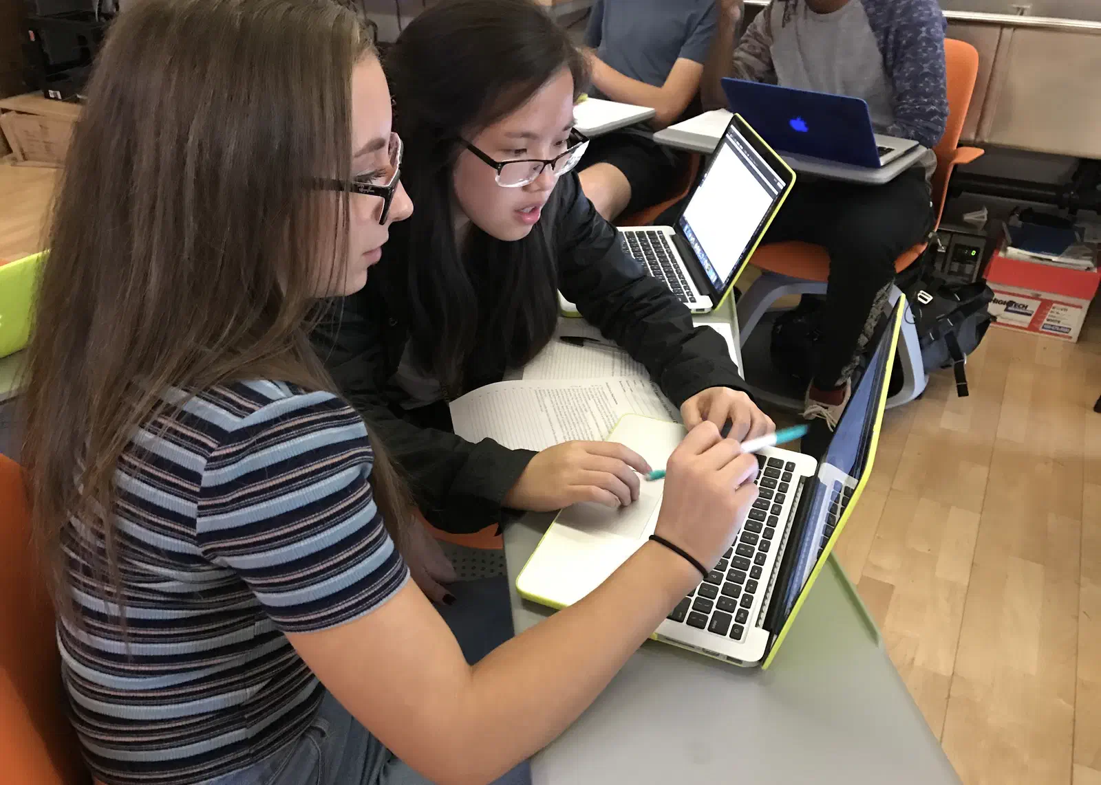 Two students working side by side on laptops at a table in the MakerLab.