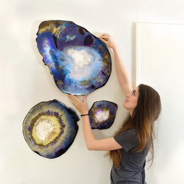 A person hanging three geode-shaped wall panels finished in blue and gold resin.