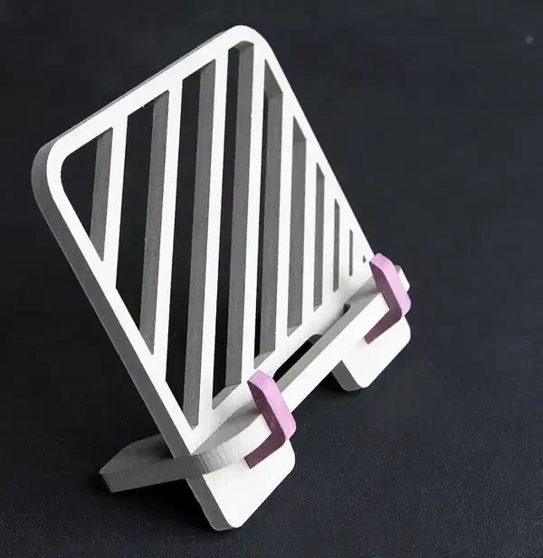 A pale MDF book stand with diagonal carved stripes and purple page hooks