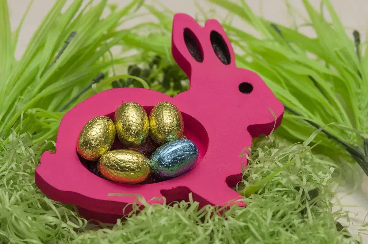 A pink wooden rabbit-shaped dish holding foil-wrapped chocolate eggs in grass