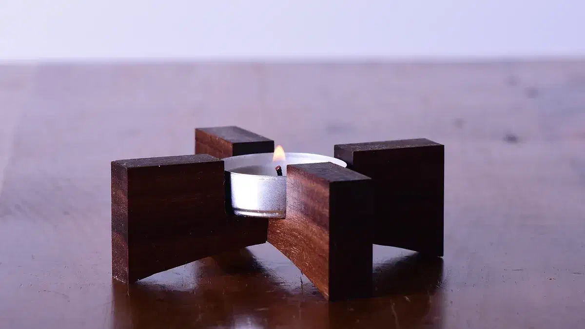 Two interlocking walnut pieces supporting a white tealight on a wooden table