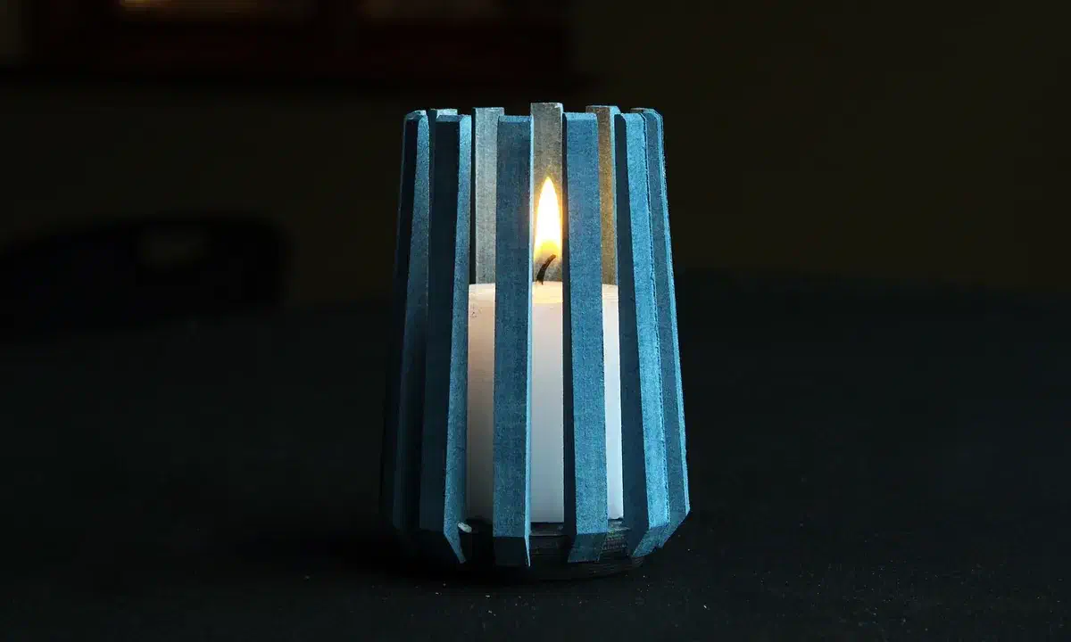A blue ribbed candle holder surrounding a white pillar candle on a dark table