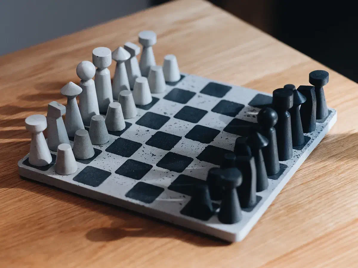 Finished chess set with pale and dark concrete pieces on a matching square board, resting on a wooden tabletop