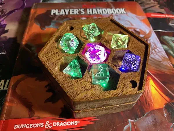 Wooden hexagonal dice box with glowing colored dice in individual pockets on a gaming book