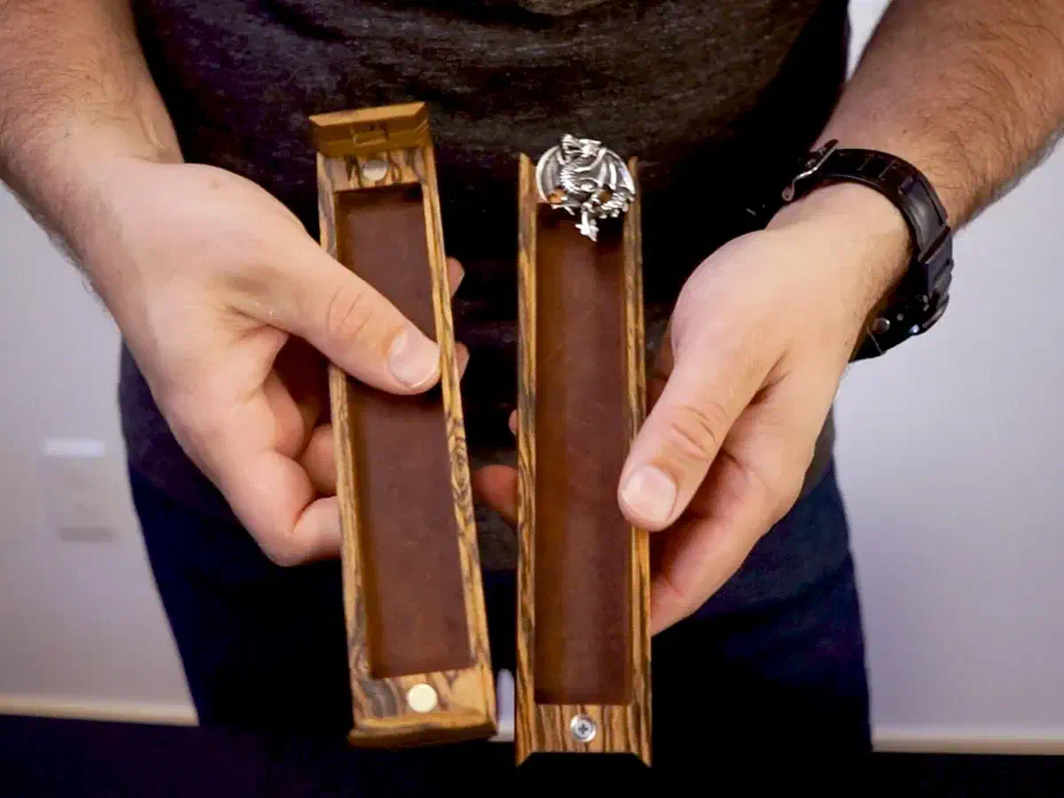 Maker holding two open leather-lined wooden dice-vault halves with magnetic lock hardware and a silver dragon decoration
