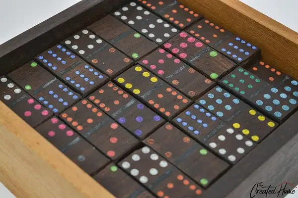 Dark wooden dominoes with brightly colored pips packed in a wooden box bearing The Created Home logo