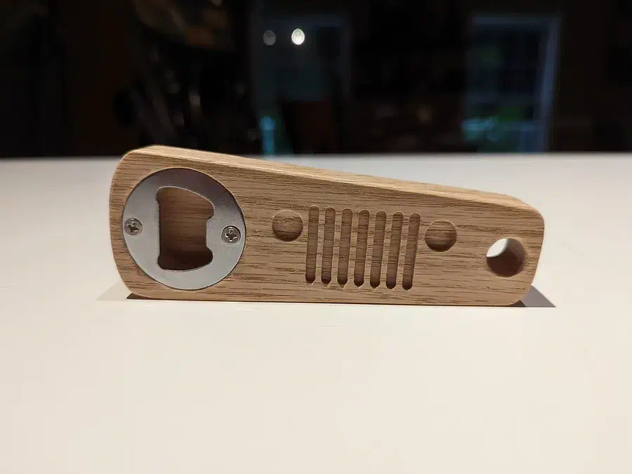 Finished wooden bottle opener shaped like a Jeep grille with a metal insert at one end