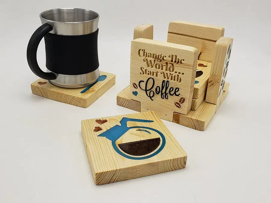 Square wooden coffee coasters with dark and blue resin-filled designs beside their wooden holder and a mug