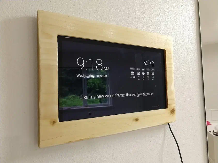 A pale wooden wall frame surrounding a Microsoft Surface tablet displaying a clock