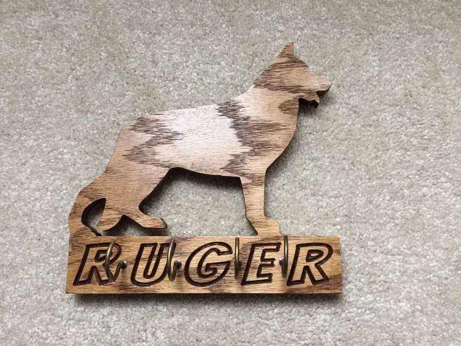 Finished wooden German shepherd silhouette above carved RUGER lettering with metal hooks between the letters