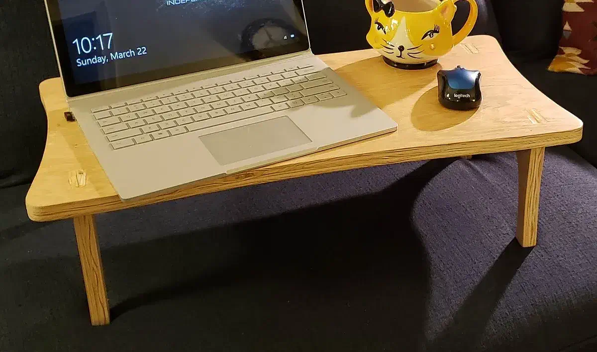 A laptop, mouse and yellow mug on a small plywood lap desk on a couch