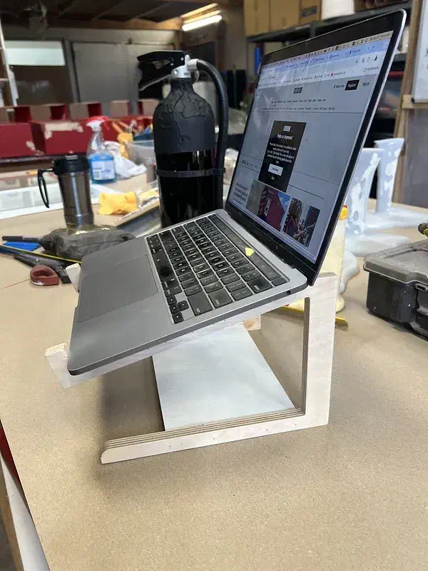 An open laptop on a pale plywood riser with rectangular side supports