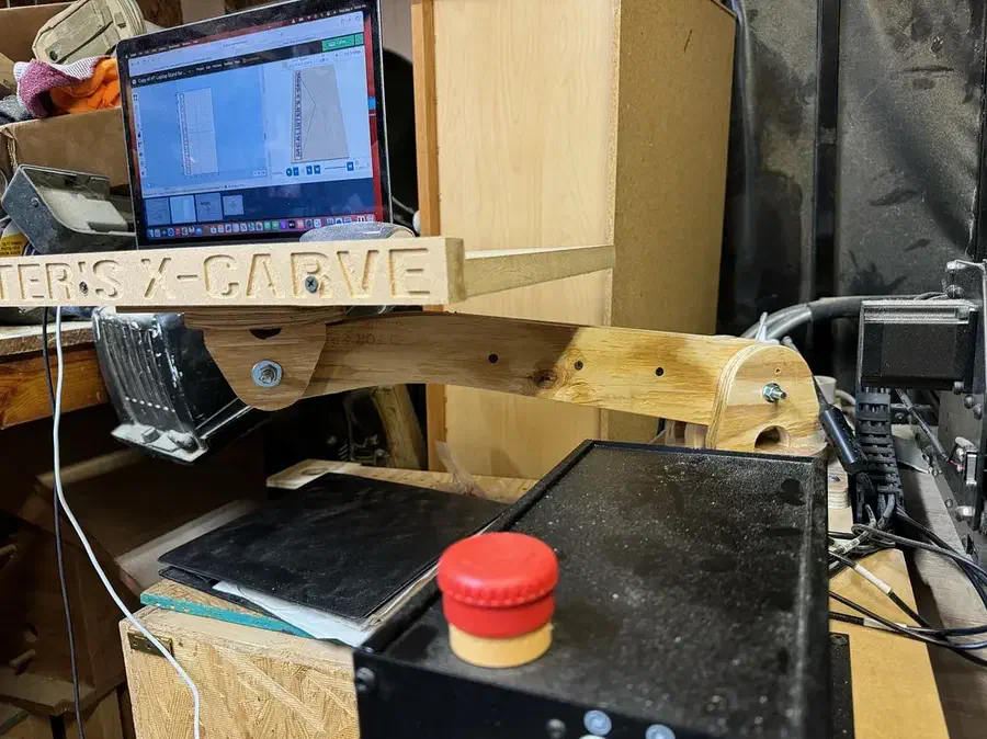 A laptop on a plywood arm beside a CNC machine with a circular joint beneath its tray