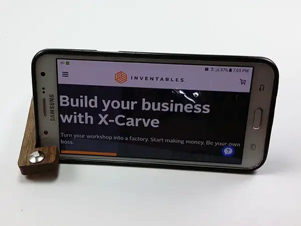 Small walnut key fob supporting a phone horizontally on a white surface