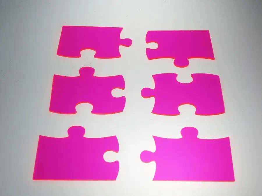 Six translucent pink acrylic jigsaw pieces separated into two columns on a pale surface