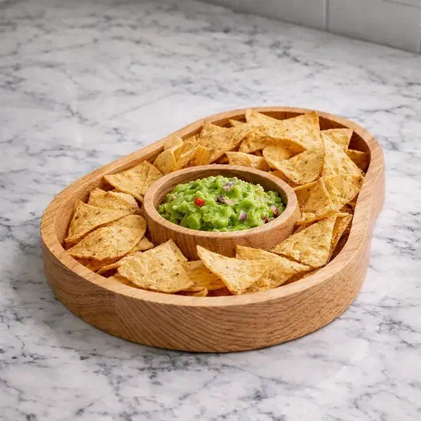 An avocado-shaped wooden dish holding tortilla chips around a central bowl of guacamole