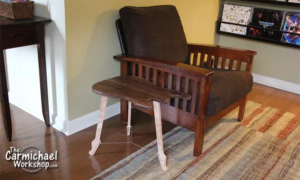 A walnut guitar-shaped side table with three pale maple legs beside a wooden armchair