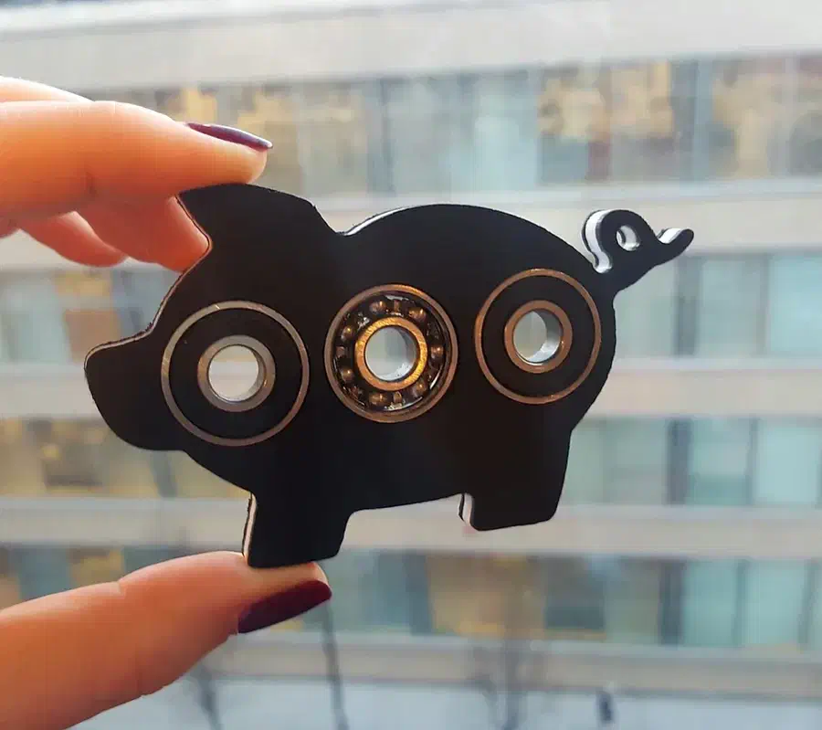 A hand holds a black pig-shaped spinner with three installed bearings against a window