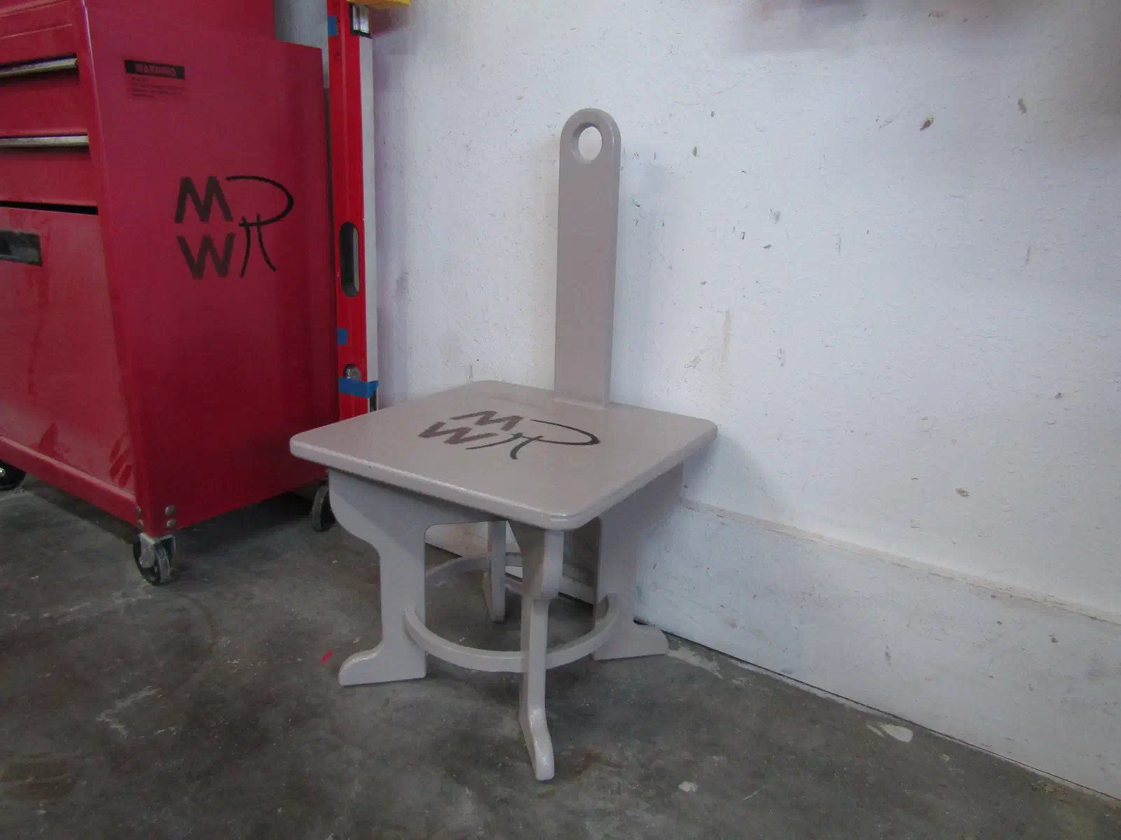 A painted gray wooden step stool with a tall upright carry handle, a square top and curved supports underneath