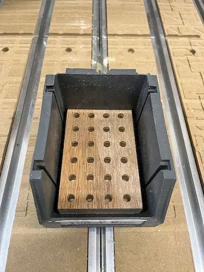 Wooden driver-bit insert with drilled rows inside a black plastic parts bin