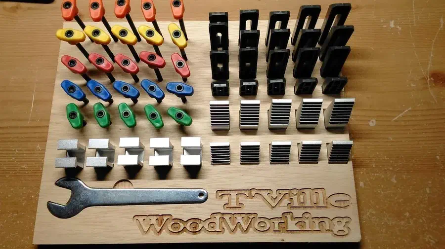 Plywood tool board holding colorful clamp screws, rows of black clamps and a metal wrench