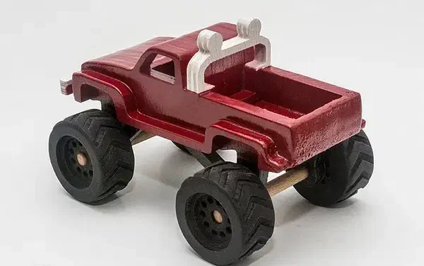 A red plywood monster truck with large black treaded wheels and a white rear roll bar