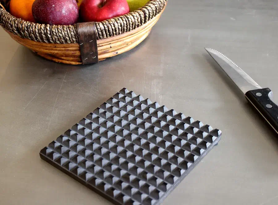 Dark Corian trivet with a raised grid of pointed studs on a kitchen counter