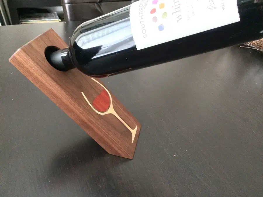 A wooden balancing wine bottle holder with a pale wine-glass outline and red inlay