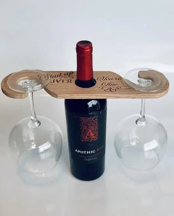 A wooden caddy resting over a wine bottle with two stemmed glasses hanging from its curved ends